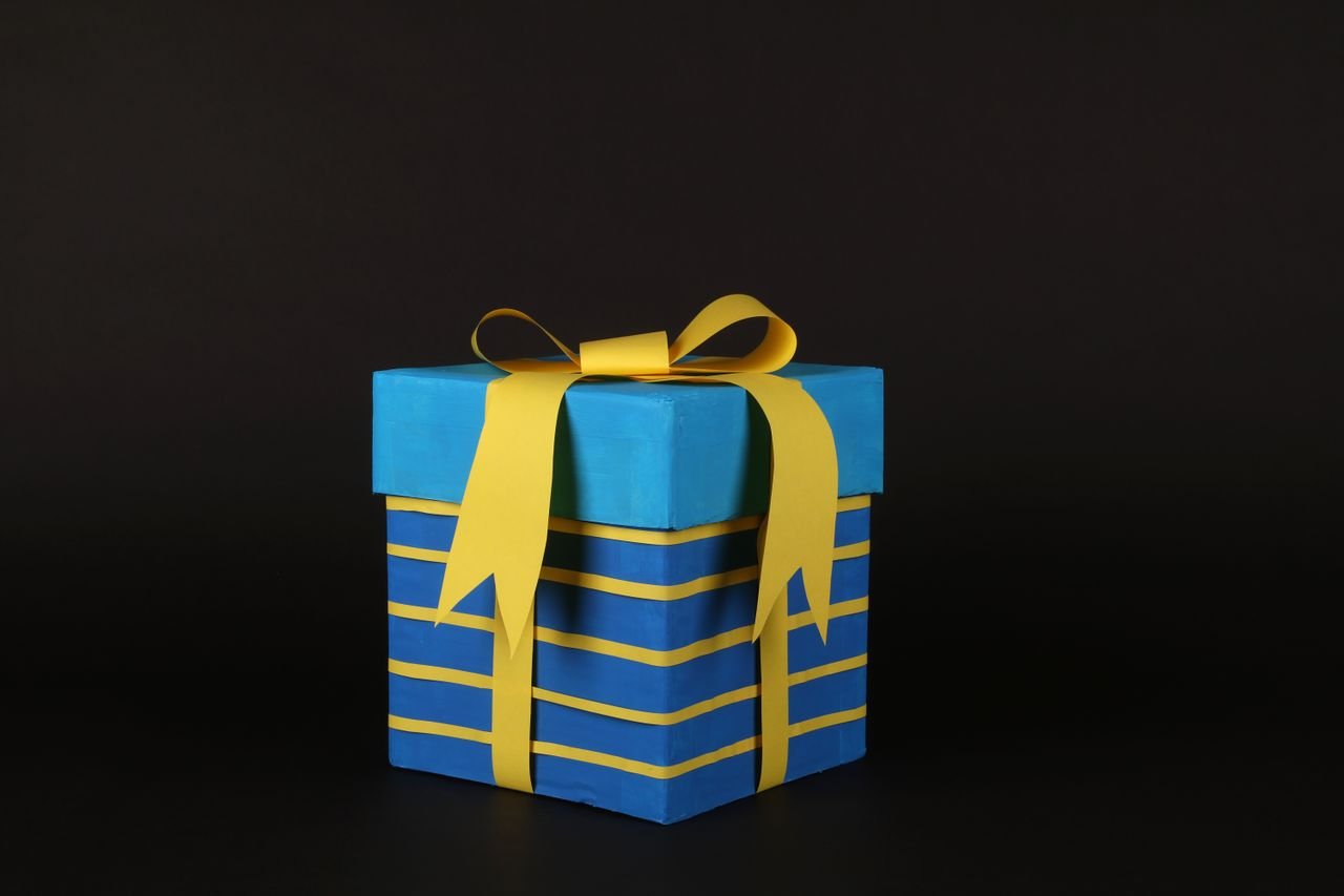 services-04 Vibrant blue gift box wrapped in yellow ribbon on black background for celebrations.