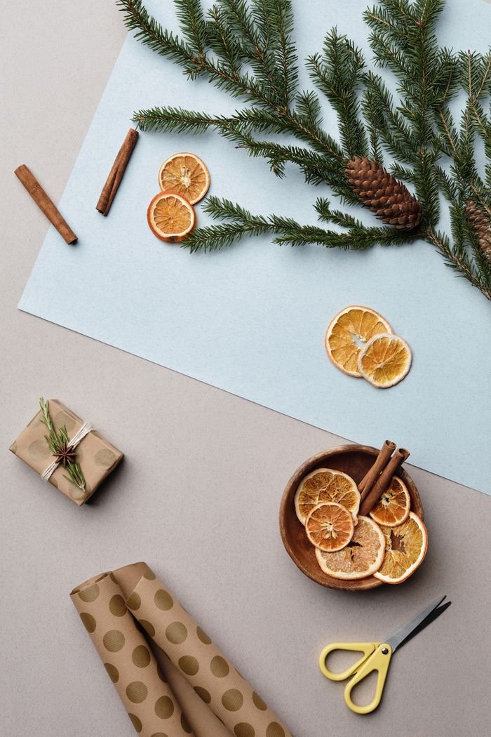 A festive flat lay features dried oranges, pine cones, cinnamon sticks, and gift wrapping items, perfect for winter themes.