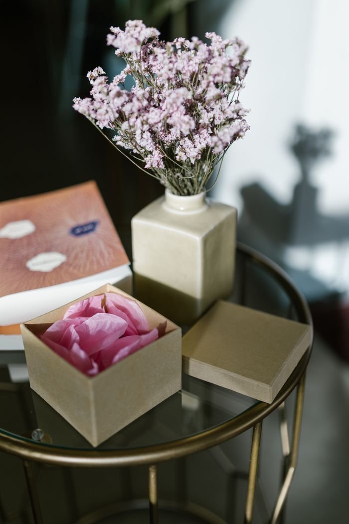 Simple yet elegant tabletop with floral vase, book, and gift box on glass table.